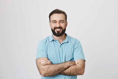 Portrait of a handsome bearded man smiling looking to the camera with his hands crossed isolated on white background. This person looks like an ordinary guy who is sincere and ready to help everyone